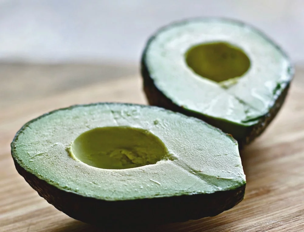 Avocado Cut In Half Laying On A Counter Top.