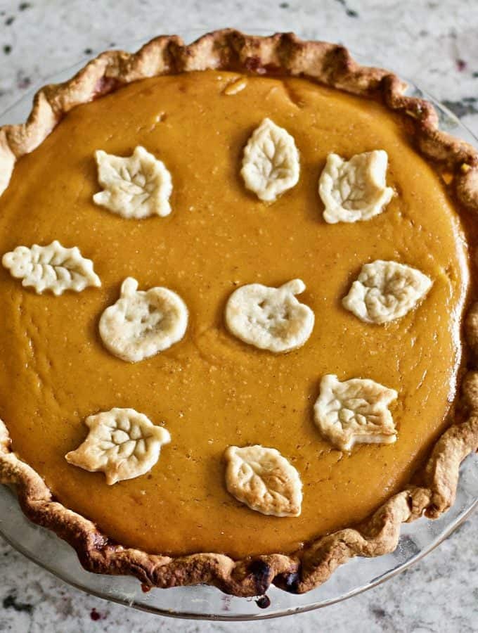 Pumpkin pie with dough cut outs on top two pumpkins and fall leaves bake in to celebrate the season