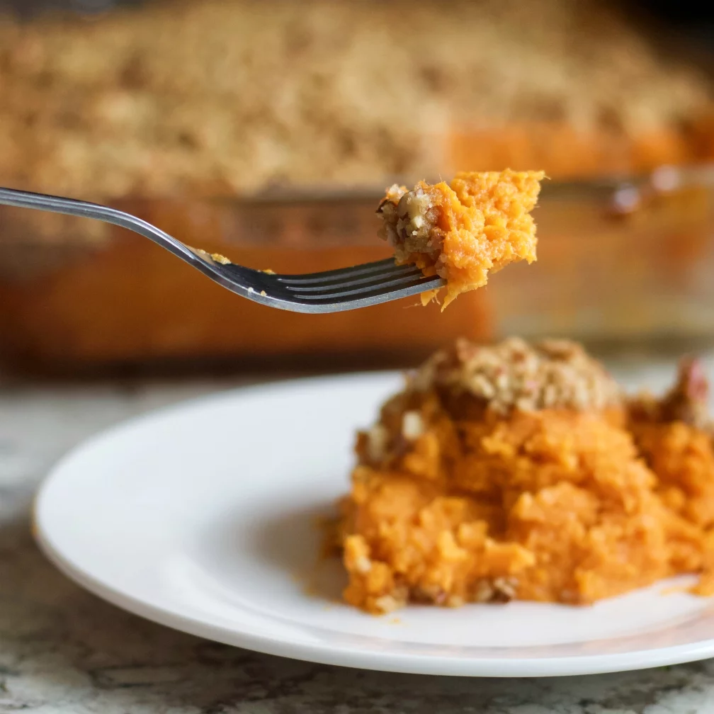 Sweet Potato Casserole Bite On A Fork With The Casserole In The Background.