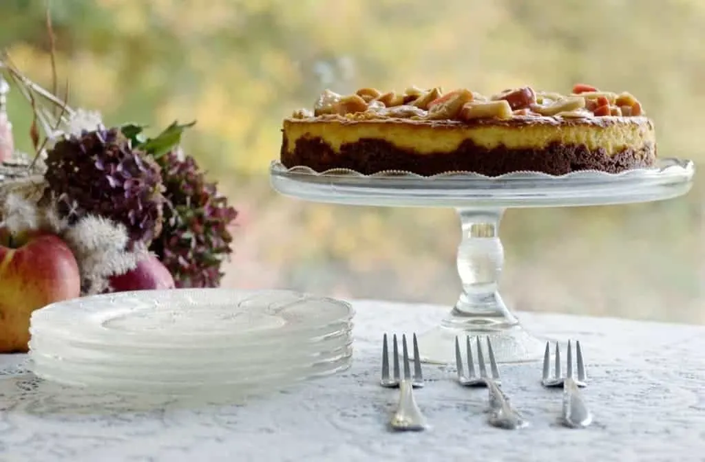Apple Pie Cheesecake Recipe 2 Apple Cheesecake On Cake Stand Resting On A Dessert Table With Fall Decorations.