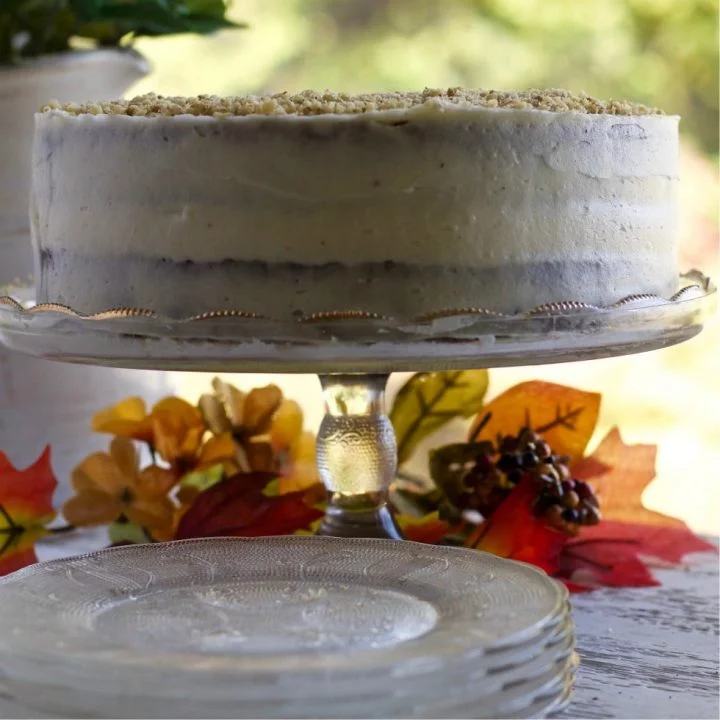 A lovely Carrot Cake with Pineapple and Pure maple Syrup on a cake stand surrounded by fall leaves