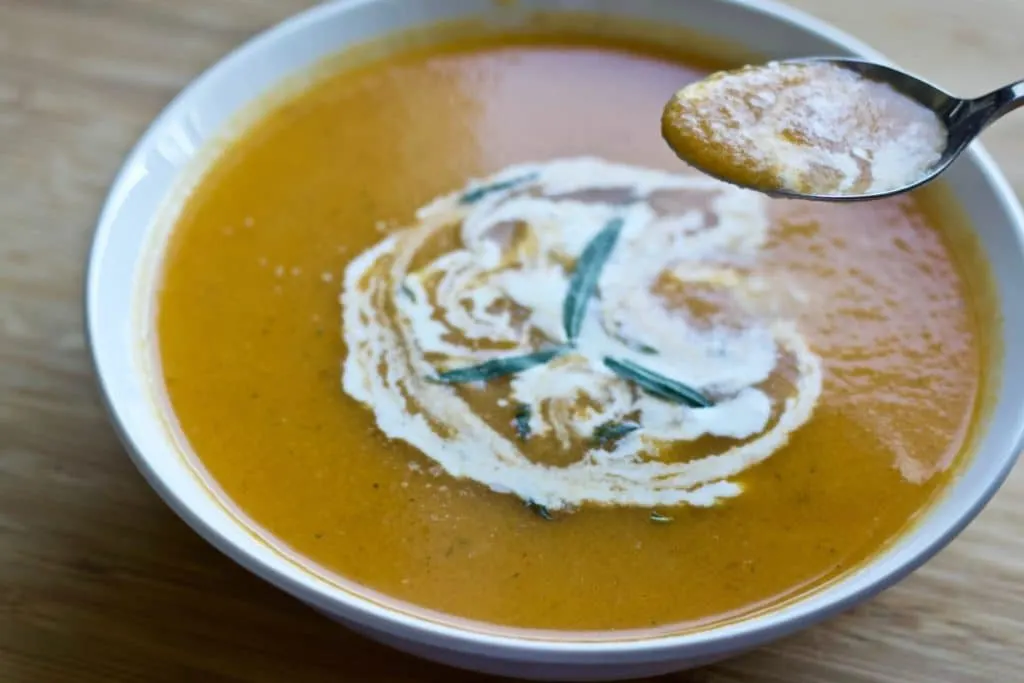 Carrot Tarragon Soup Garnished With Fresh Tarragon And Cream In A White Bowl