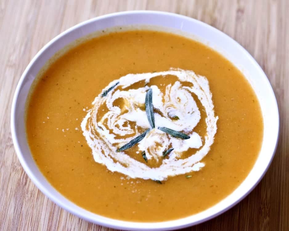 Carrot Tarragon Soup Garnished With Fresh Tarragon And Cream In A White Bowl