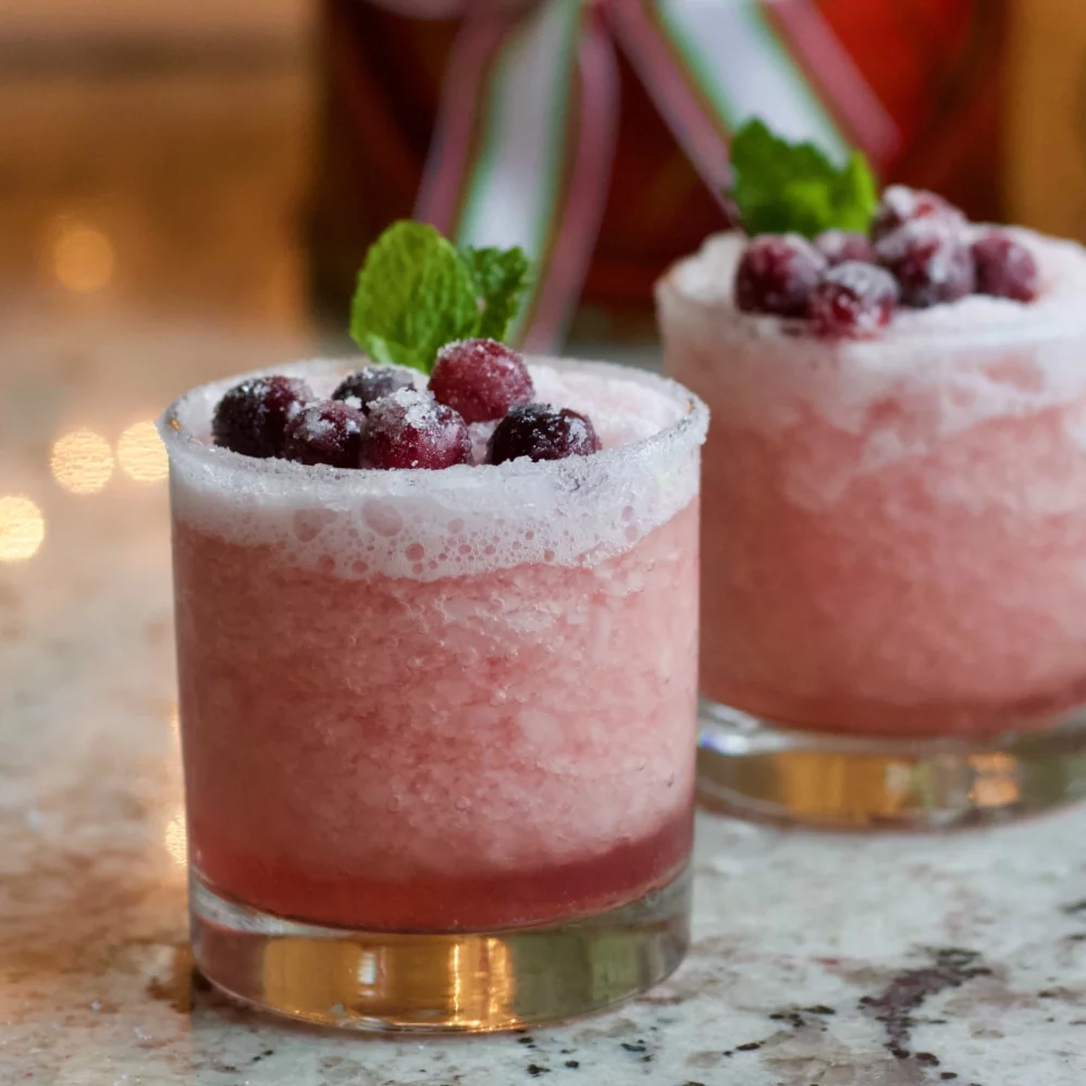 Two Frosty Cranberry Margaritas Garnished With Sugared Cranberries And Mint Leaves.
