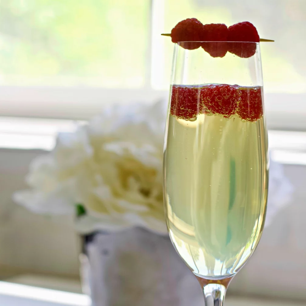 Limoncello Prosecco Garnished Next To A White Flower In Front Of A Window.