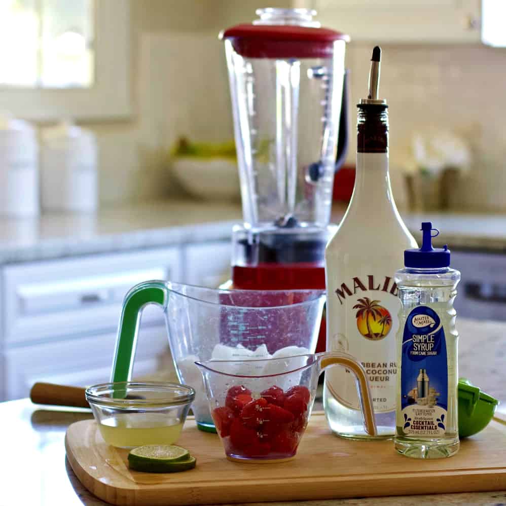 The Ingredients For This Drink Sitting On A Wooden Board With A Blender.