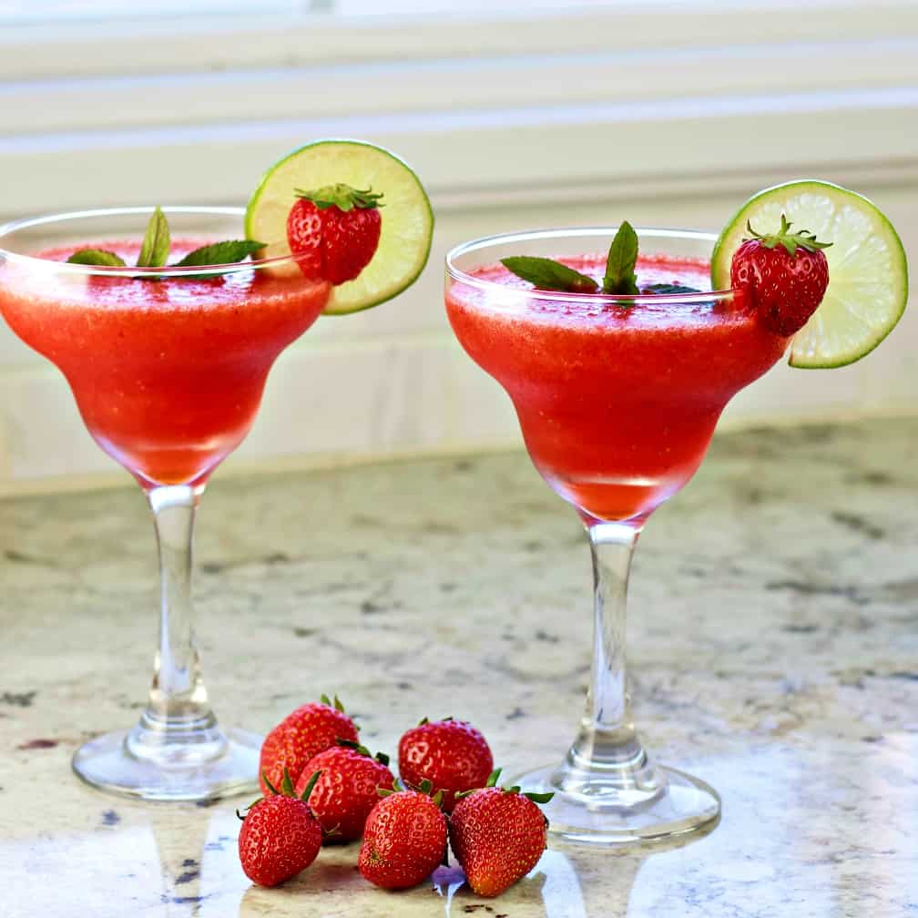 Frozen Strawberry Daiquiris With Whole Fresh Strawberries On The Counter Around Them.