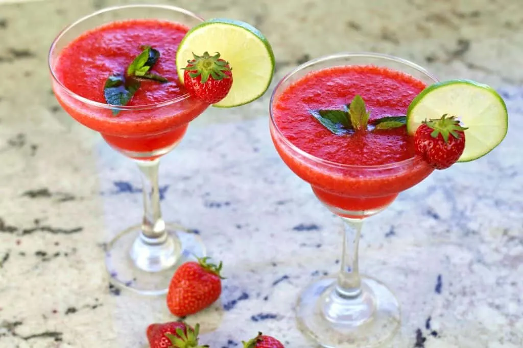 Two Strawberry Daiquiris Garnished With Mint Leaves, Lime Wheels And A Whole Fresh Strawberry.