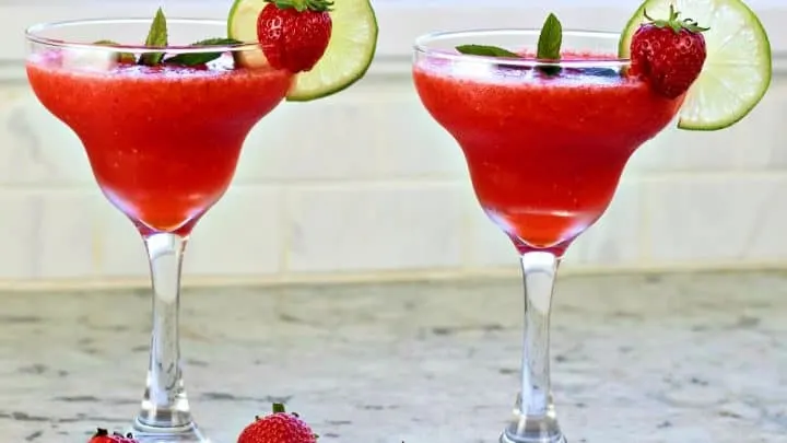 Two Strawberry Daiquiris Garnished With Lime Wheels And Whole Strawberries