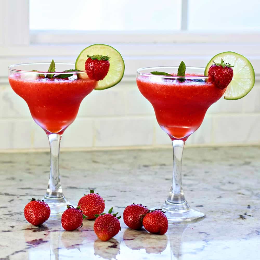Two Strawberry Daiquiris Garnished With Lime Wheels And Whole Strawberries