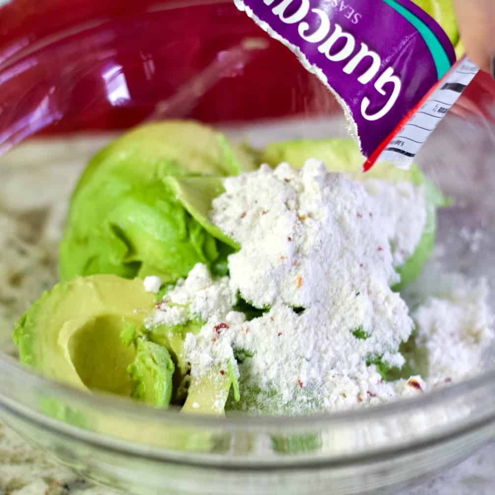 Adding The Guacamole Seasoning To Avocado-Layered Bean Dip.