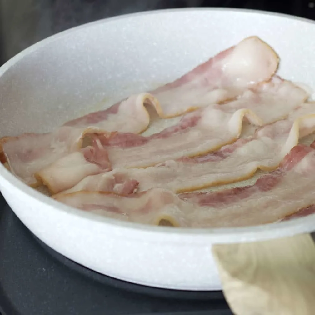 Cooking Bacon In A White Skillet