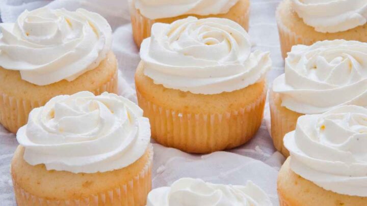 a group of vanilla cupcakes on parchment with white buttercream frosting
