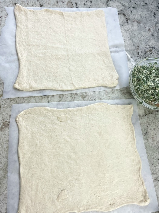 Two Pizza Crusts Laying Side By Side On Parchment Paper Ready For Shaping.