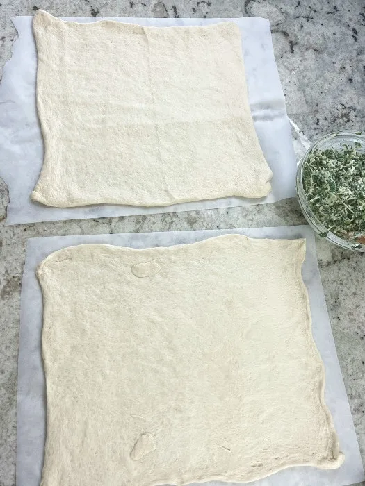 Two Pizza Crusts Laying Side By Side On Parchment Paper Ready For Shaping.