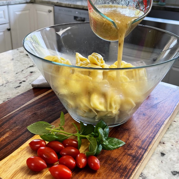 Twisted Caprese Tortellini Pasta Salad 6 Pouring Dressing Onto Tortellini In Salad Bowl