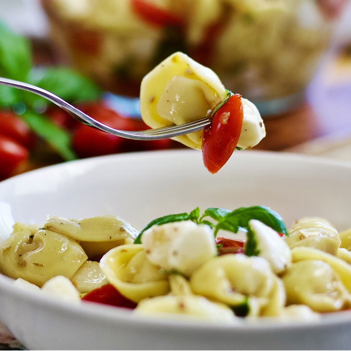 forkful of tortellini caprese salad over bowl of salad