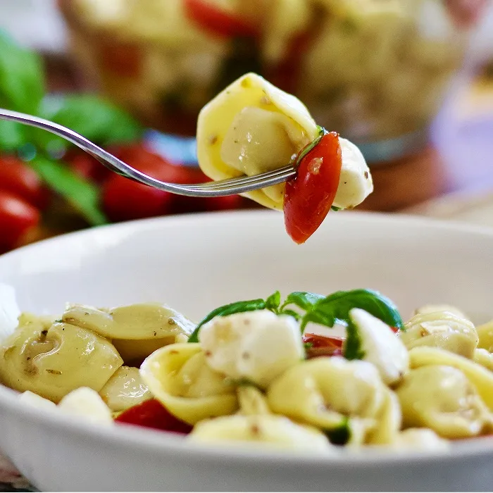 Forkful Of Tortellini Caprese Salad Over Bowl Of Salad