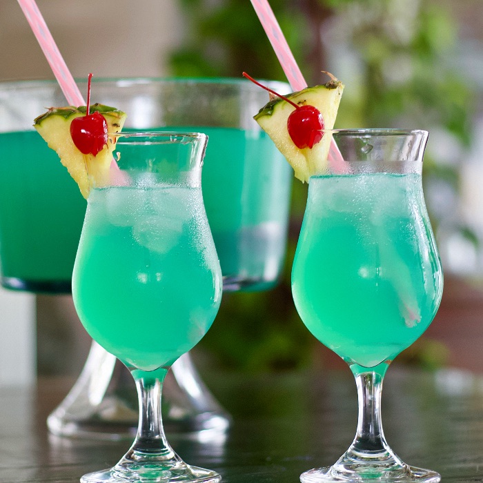 blue lagoon punch bowl with two garnished hurricane glasses with punch