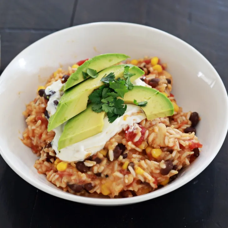 mexican chicken and rice in a white bowl with avocado slices on top