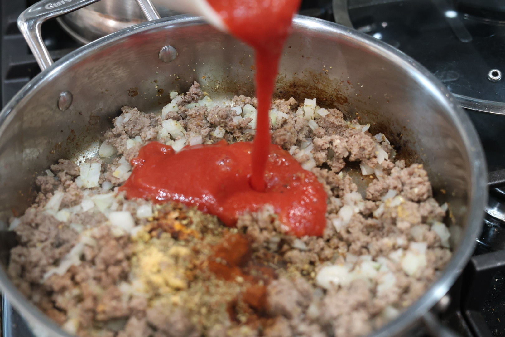 Ultimate Cheesy Beef and Shells Dinner 7 pouring in tomato sauce. cheesy beef and shells dinner in a skillet
