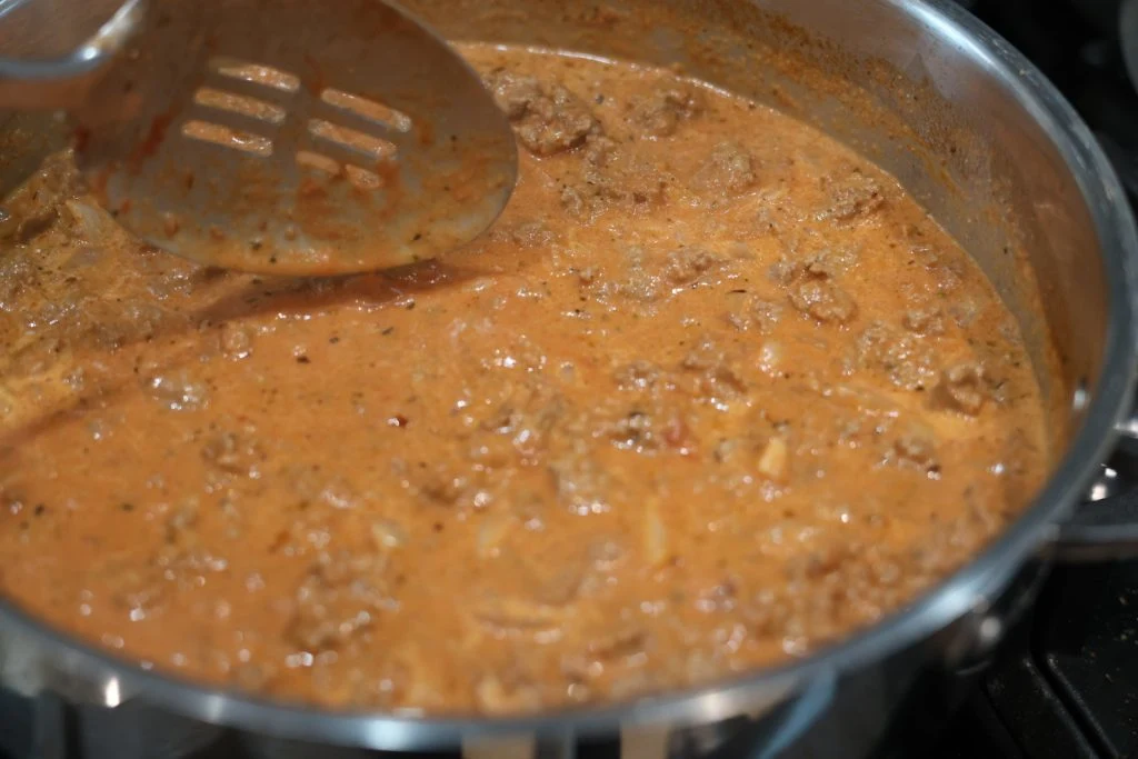 stirring sauce in a skillet for cheesy beef and shells