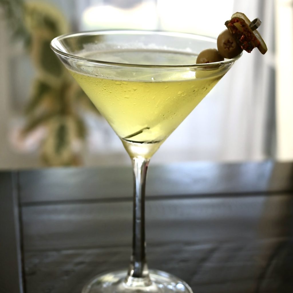 Absolut Tabasco Vodka Martini (Spicy Pickle Martini Recipe) 2 spicy Pickle-Tini in a chilled martini glass on a black table backlit by a window.